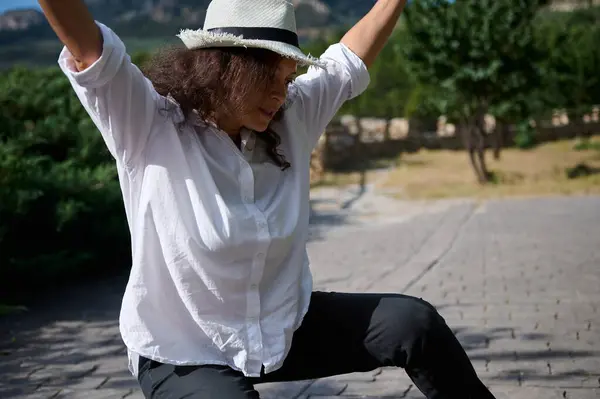 stock image A woman in a white shirt and hat practicing yoga outdoors. She appears focused and serene, surrounded by greenery and nature. Sunny day, peaceful outdoor activity.