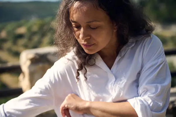 stock image A pensive woman in a white shirt enjoys a tranquil moment outdoors, surrounded by natural scenery. She appears relaxed and contemplative.