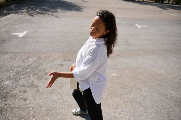 stock image Woman in white shirt dancing outdoors in a parking lot on a sunny day. She appears carefree and joyful, basking in the sunlight.