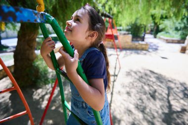 Neşeli genç çocuk güneşli bir parktaki renkli oyun parkına tırmanırken dışarıda oyun ve maceranın tadını çıkarıyor..