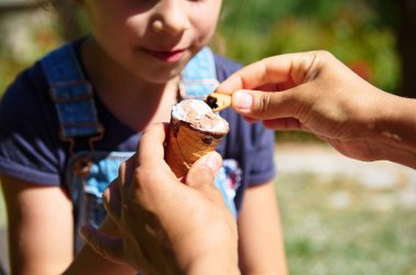 Bir çocuğun dondurma külahını tutarken, diğer elin üstüne bir şey eklerken yakın plan fotoğrafı. Yaz, aile ve açık hava temalı projeler için mükemmel..
