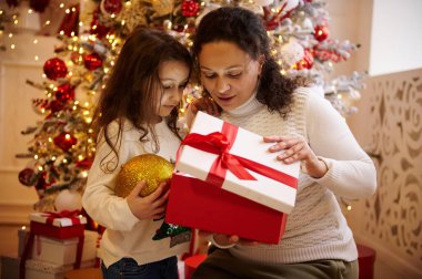 Bir anne ve kızı, Noel hediyesini, süslenmiş ve iyi ışıklandırılmış bir Noel ağacının yanında, sevgi ve heyecanla kutluyor..