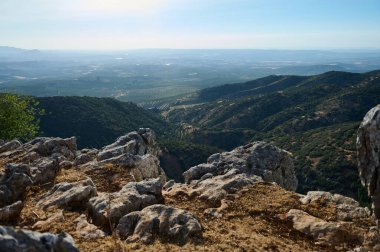 Bereketli yeşil bir dağ sırasının ve kayalık bir uçurumdan görünen geniş tarım arazisinin çarpıcı panoramik manzarası berrak mavi gökyüzünün altında..