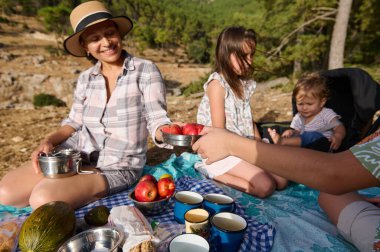 Aile açık havada taze meyve ve içeceklerle harika bir piknik yapıyor. Ebeveynler ve çocuklar güneşli bir günde birlikte iyi vakit geçiriyorlar..