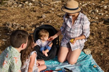 Güneşli bir günde dışarıda piknik yapan dört kişilik bir aile. Bir kadın bebeğini beslerken iki çocuk yan yana oturup kaliteli aile zamanlarının tadını çıkarıyor..