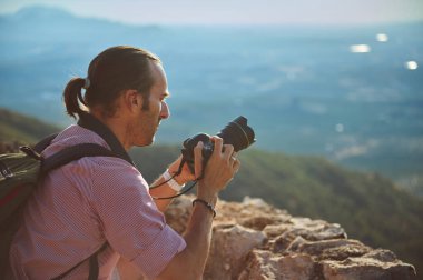Güzel bir dağ manzarasının fotoğrafını çeken bir fotoğrafçının yan görüntüsü profesyonel bir kamerayla odaklanıyor. Sahne, doğa fotoğrafçılığının ve doğa macerasının özünü yakalıyor..
