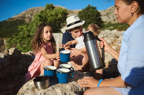 stock image Family having a relaxing outdoor picnic, sharing hot drinks. The image captures togetherness, nature, and relaxation on a sunny day, with children and adults bonding.