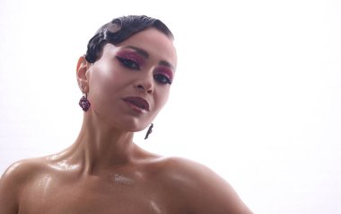 Cesur makyaj ve şık mücevherlerle poz veren kendine güvenen bir manken. Basit beyaz bir arka plana zarafet ve cazibe yayıyor..