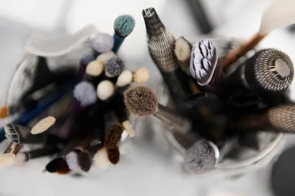 stock image Top view of various makeup brushes in glass containers, showcasing tools for professional beauty, cosmetics, and personal care. Ideal for beauty studio, salon, makeup tutorial, and professional kits.