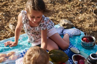 Genç kız ve bebek güneşli bir günde pikniğin tadını çıkarıyorlar. Etrafı yiyeceklerle çevrili bir battaniyeye otururlar. Doğadaki neşe ve birlikteliği paylaşırlar..