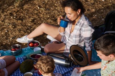 Aile açık havada piknik yapıyor, yemek yiyor, termos yiyor ve güneşli bir günde birlikte rahatlıyor..