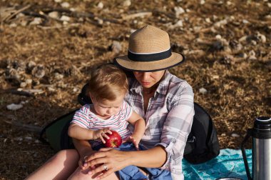 Bir anne ve çocuk piknikte birlikte güzel vakit geçiriyorlar. Çocuk bir elma tutuyor. Aile bağı, açık hava aktiviteleri ve ebeveyn-çocuk ilişkileri ile ilgili konular için ideal.