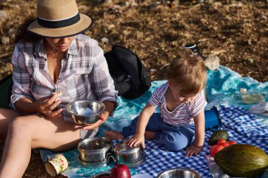 Güneşli bir günde, bir anne ve bebeği bir pikniği paylaşır, battaniyenin üzerinde oturur ve birlikte güzel vakit geçirirler..