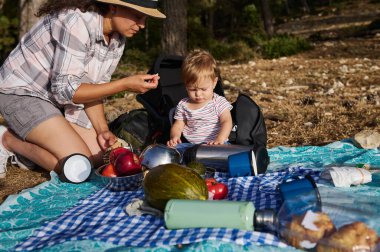 Bir anne ve yavrusu açık havada taze meyve ve sebzelerle battaniyede piknik yapıyorlar. Aile bağının ve doğanın özünü yakaladığımız an..