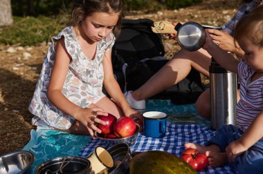 Çocuklar güneşli bir günde dışarıda taze elmalar ve atıştırmalıklarla pikniğin tadını çıkarırlar. Neşeli atmosfer ve doğal ortam sıcak ve neşeli bir deneyim yaratıyor..