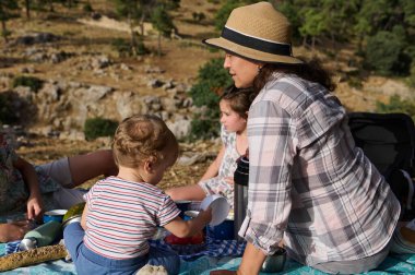Anne ve çocuklar doğa ve dağlarla çevrili manzaralı bir yerde piknik yaparken birlikte kaliteli zaman geçiriyorlar..