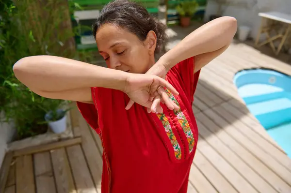 stock image A woman in a red dress savoring a peaceful moment by the poolside on a sunny day. The serene environment highlights relaxation and joy.