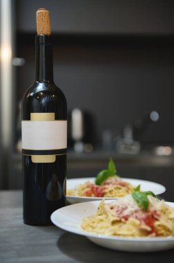 İki tabak domates soslu ve fesleğenli makarnanın yanında mantarlı bir şişe kırmızı şarap sıcak bir akşam yemeği atmosferi yaratır..