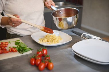Mutfakta domates soslu makarna hazırlayan kişi. İçinde domates ve fesleğen gibi taze malzemeler var..