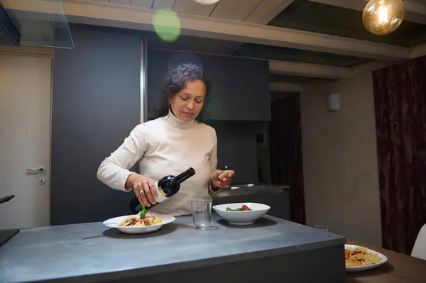 stock image Woman preparing dinner and pouring wine in a modern kitchen. Scene with a cozy dining setup and an atmosphere of relaxation and enjoyment.