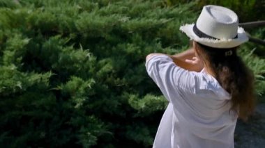 Açık havada yemyeşil çalıların yanında duran beyaz şapkalı ve beyaz gömlekli bir adam. Sahne, huzur, rahatlama ve doğayla bağlantıyı iletir..