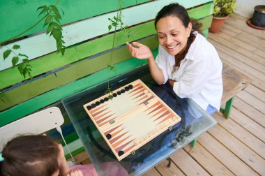 Anne ve kızı güneşli bir günde dışarıda tavla oynuyorlar. Aile bağları, kahkahalar ve kaliteli zaman geçirme anı..
