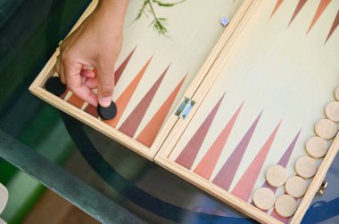 Bir el, açık hava oyun oturumu sırasında tavla tahtasına oyun taşını yerleştirirken. Boş zaman, strateji ve eğlence temaları için ideal.