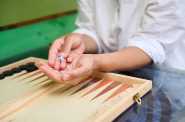 Zar tutan ellerin yakın çekimi, ahşap bir tahtada tavla oynarken yuvarlanmaya hazırlanmak. Resim, masa oyunlarının ve boş zaman aktivitelerinin özünü yakalar.