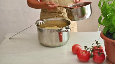 A person cooking Italian pasta, adding sauce from a pot with fresh tomatoes and basil on the table, showcasing a cozy home-cooking setting. clipart