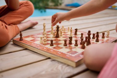 İki çocuk tahtadan bir güvertede satranç oynamaktan zevk alıyor. Açık havada bir yaz günü strateji, konsantrasyon ve eğlence..