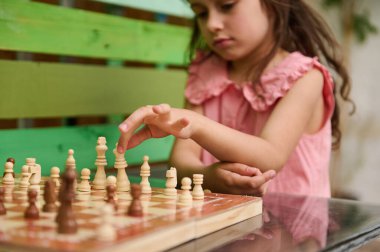 Pembe elbiseli genç bir kız yoğun bir şekilde stratejik bir satranç hamlesi yapmaya odaklanmış. Sahne, çocukluk konsantrasyonu, zeka ve stratejik düşüncenin özünü yakalar..
