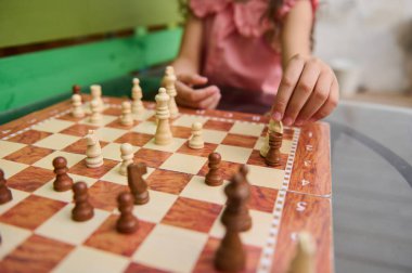 Satranç maçına katılan bir çocuk, tahta bir satranç tahtasında satranç taşlarını oynatıyor. Görüntü strateji ve bilişsel beceri gelişimini vurguluyor.