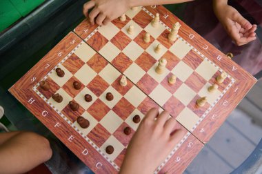 Ahşap bir satranç tahtasında stratejik bir satranç oynayan çocukların en iyi görüntüsü, el ele tutuşan taşları, takım çalışmasını ve açık hava çarpışmasını gösteriyor..