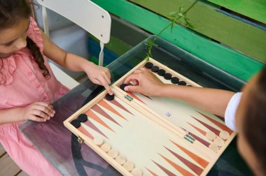 Dışarıda tavla oynayan bir çocuk ve yetişkin. Gelişigüzel ayarlar ve paylaşılan aktiviteler bir aile bağı ve rahatlama hissi yaratıyor..