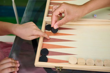 Tahta bir tahtanın üzerinde tavla oynayan iki elin yakın çekimi. Görüntü strateji, konsantrasyon ve aile bağlarını yakalar..