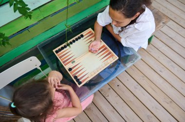 Bir anne ve kızın, rahat ve açık havada, ahşap bir güvertede tavla oynamalarının keyfini çıkardıkları tepeden bakıldığında..
