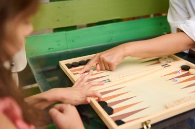 Tavla oynayan iki kişinin detaylı bir görüntüsü. Eller dama oynamaya odaklansın. İçerde boş zaman aktivitesi.