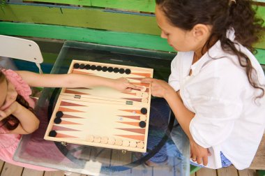 İki çocuk eğlenceli bir tavla oyununda, dışarıda canlı, renkli bir masada oynuyorlar. Aile zamanı, oyun ve geleneksel oyun temaları için mükemmel..