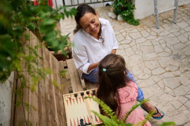 Bir anne ve kızı dışarıda sakin bir ortamda tavla oynarken keyifli bir anı paylaşıyorlar. Sahne, aile bağlarının ve boş zamanların özünü yakalıyor..