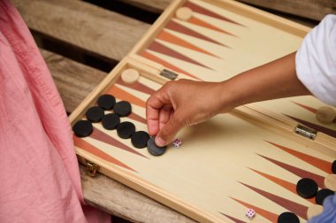 Tavla oynayan, tahta bir tahtanın üzerinde siyah parçaları hareket ettiren birinin yakın çekimi. Açık hava aktivitesi, strateji ve eğlence konsepti.