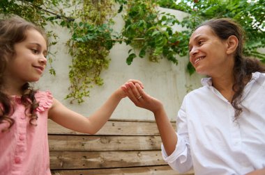 Bir anne ve kızı el ele tutuşurken ve huzurlu bir bahçe ortamında gülümserken birbirlerine karşı sevgi dolu bir an. Aile bağları, aşk ve mutluluk taşınır..