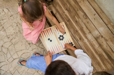 Anne ve kızı açık havada tavla oynuyorlar. Ahşap bank ve taş zemin rahat ve rahatlatıcı atmosferi arttırır..