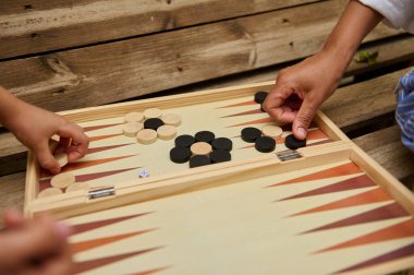 Ahşap bir yüzey üzerinde, bir tavla oyununda el ele tutuşan eller. Eğlenceli ve stratejik bir masa oyunu deneyimi.