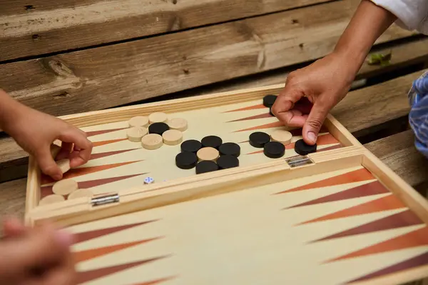 stock image Close-up of hands engaging in a backgammon game outdoors on a wooden surface. A fun and strategic board game experience.