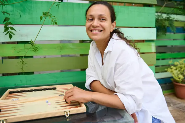 stock image A cheerful woman having a good time playing backgammon outdoors. She is smiling and looks relaxed while enjoying the casual game.