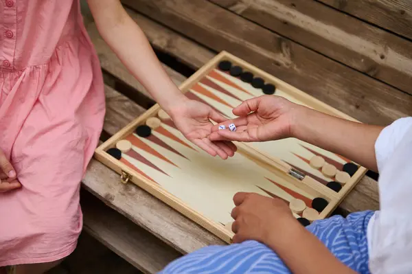 stock image Two individuals enjoying a game of backgammon on a wooden board. The outdoor setting and casual attire suggest a leisurely summer day.