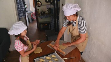 Bir anne ve kız sıcak bir mutfakta birlikte kurabiye pişirmekten hoşlanırlar. İkisi de aşçı şapkaları ve önlükleri takıyor, öğrenip kaynaşıyorlar..