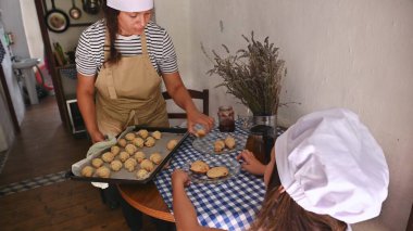 Bir anne ve çocuk sıcak bir ev mutfağında birlikte hamur işi pişirmekten hoşlanırlar. Çocuk annesinin fırından yeni çıkmış kruvasanları çıkarmasını izliyor..