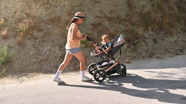 Genç bir anne bebeğiyle güneşli bir günde bebek arabasında koşar, açık hava egzersizinden ve birlikte iyi vakit geçirmekten zevk alır..