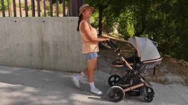 Güneşli bir günde bebeğiyle bir bebek arabasında gezmekten hoşlanan bir kadın açık hava eğlencesi ve anneliği yansıtıyor..